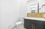 This modern bathroom features a sleek vanity with gold hardware and a white countertop, complemented by a stylish tiled backsplash.