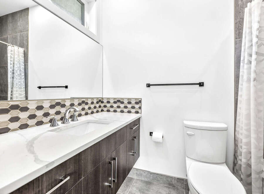 This modern bathroom features a sleek vanity with a white countertop and dark wood cabinets, complemented by a stylish hexagonal tile backsplash.
