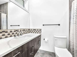 This modern bathroom features a sleek vanity with a white countertop and dark wood cabinets, complemented by a stylish hexagonal tile backsplash.