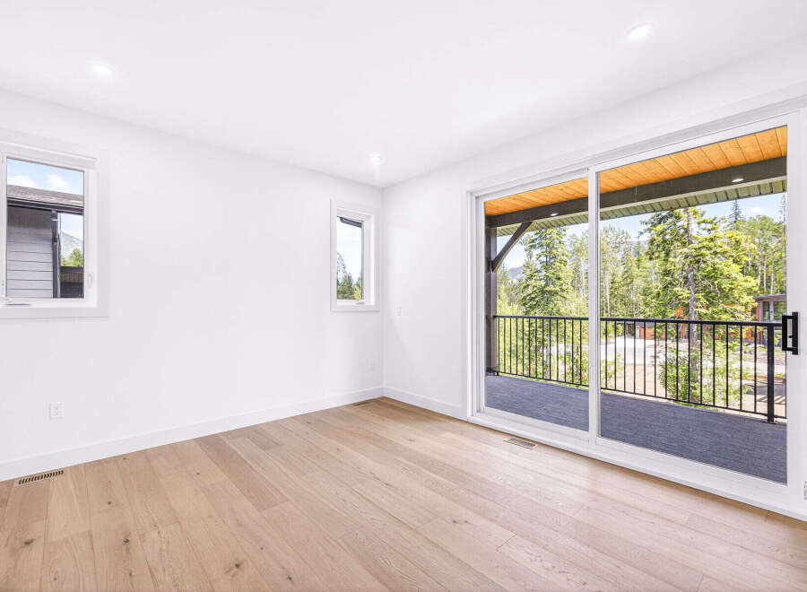 Step into this bright and airy bedroom, featuring a large sliding glass door that opens to a scenic balcony with stunning mountain and forest views.