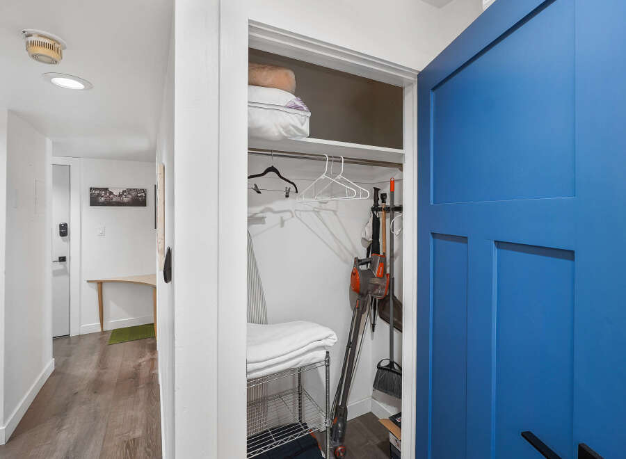 Discover convenient storage solutions with this well-organized closet, featuring a vacuum cleaner, broom, and ironing board.