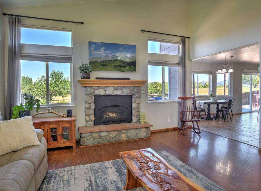 Experience breathtaking mountain views from this stunning living room, featuring a grand stone fireplace and a large picture window.