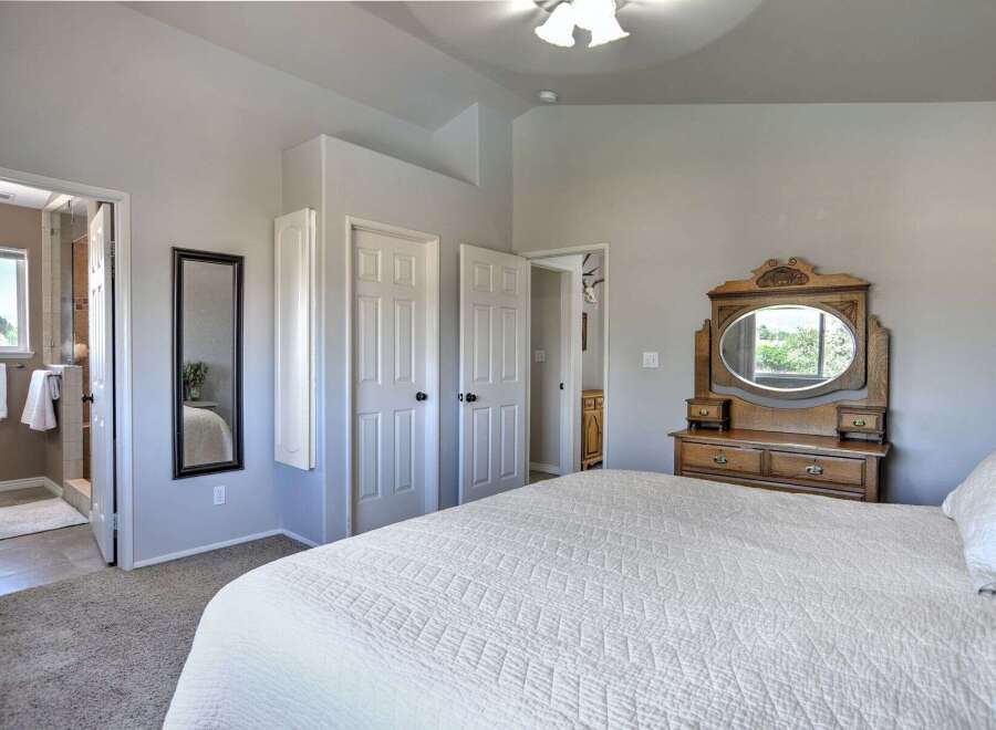 This spacious bedroom features a large white quilted bed, a vintage wooden dresser with an oval mirror, and ample closet space.