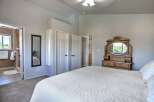 This spacious bedroom features a large white quilted bed, a vintage wooden dresser with an oval mirror, and ample closet space.