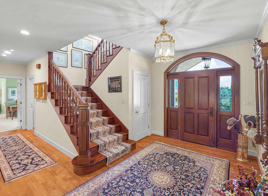 Step into a grand foyer featuring a beautiful wooden staircase with a patterned runner and a large oriental rug.