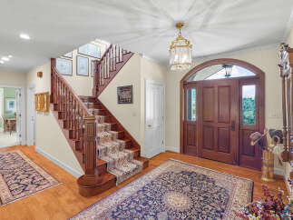 Step into a grand foyer featuring a beautiful wooden staircase with a patterned runner and a large oriental rug.