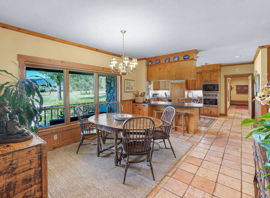Enjoy meals with a view in this charming dining area, featuring a rustic wooden table and chairs set against a backdrop of expansive windows overlooking a lush landscape.