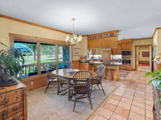 Enjoy meals with a view in this charming dining area, featuring a rustic wooden table and chairs set against a backdrop of expansive windows overlooking a lush landscape.
