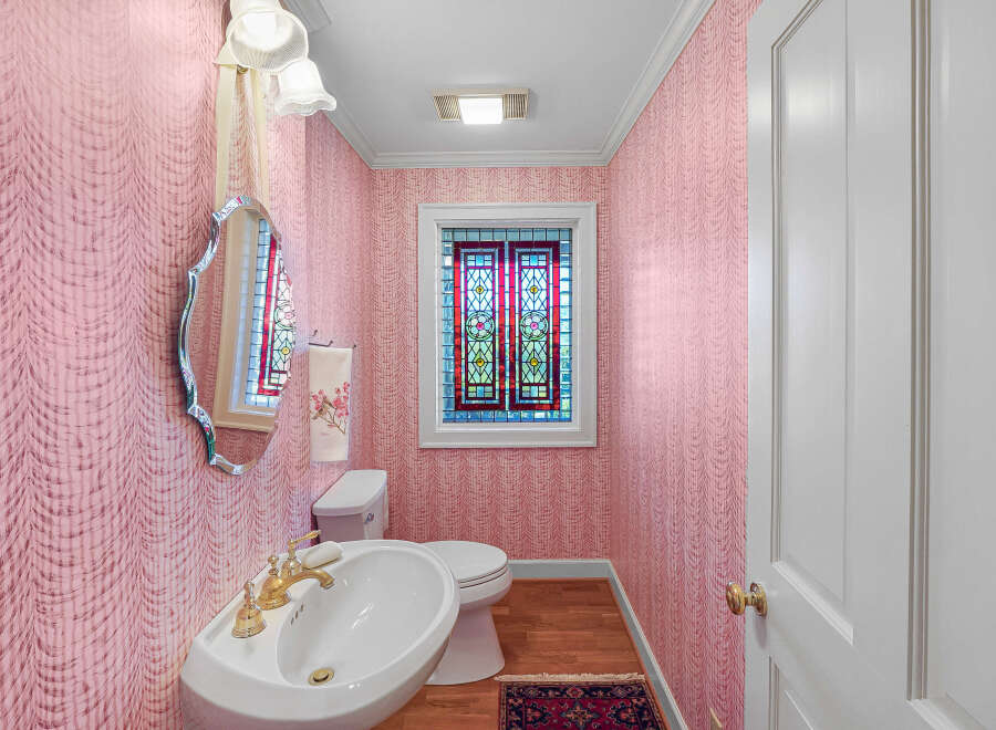 Step into this charming powder room featuring elegant pink damask wallpaper and a decorative stained-glass window that adds a touch of vintage flair.