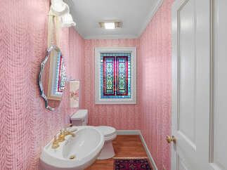 Step into this charming powder room featuring elegant pink damask wallpaper and a decorative stained-glass window that adds a touch of vintage flair.