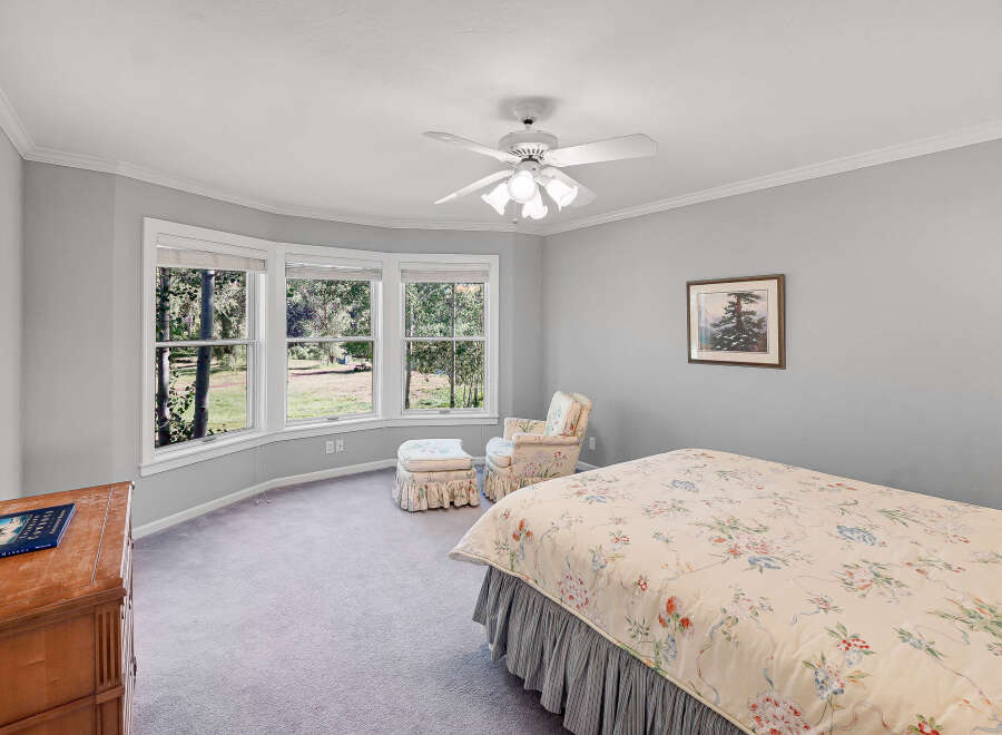 This charming bedroom features a comfortable bed with a floral comforter and a matching armchair with an ottoman, perfect for relaxation.