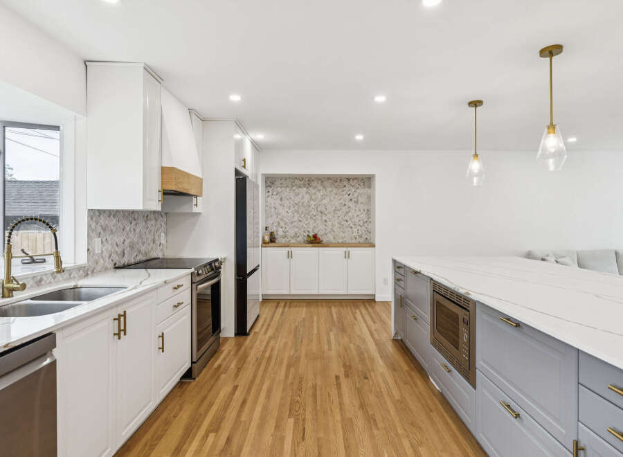 Experience modern luxury in this stunning kitchen, featuring sleek white cabinetry, a striking marble backsplash, and a spacious island with a built-in microwave.