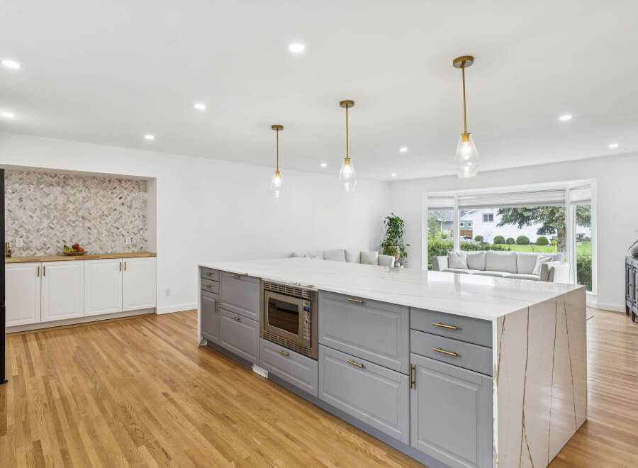 Experience modern luxury in this stunning kitchen, featuring a spacious island with a waterfall countertop and sleek gray cabinetry.