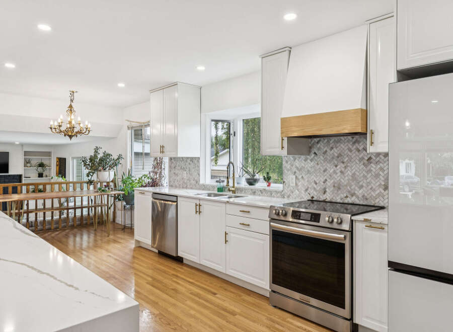 Experience modern luxury in this stunning kitchen, featuring sleek white cabinetry, a herringbone tile backsplash, and a sophisticated wooden range hood.