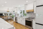 Experience modern luxury in this stunning kitchen, featuring sleek white cabinetry, a herringbone tile backsplash, and a sophisticated wooden range hood.