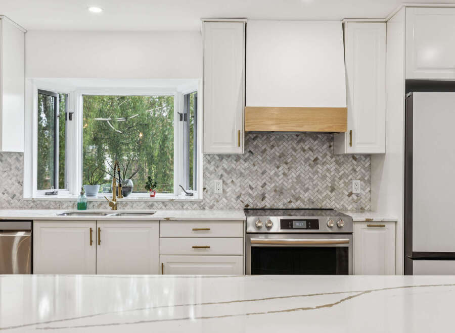 Experience modern elegance in this stunning kitchen, featuring sleek white cabinetry and a captivating herringbone tile backsplash.