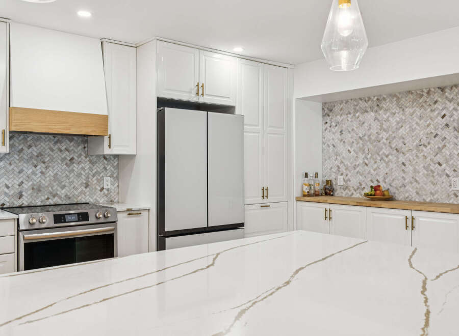 Experience modern luxury in this stunning kitchen, featuring a sleek stainless steel refrigerator and a sophisticated herringbone tile backsplash.