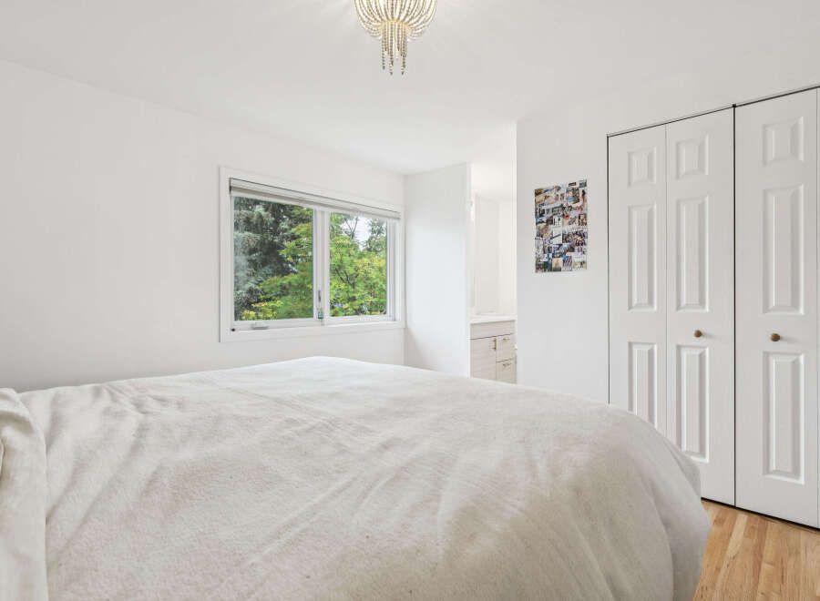 This bright and airy bedroom features a large window offering serene views of lush greenery.