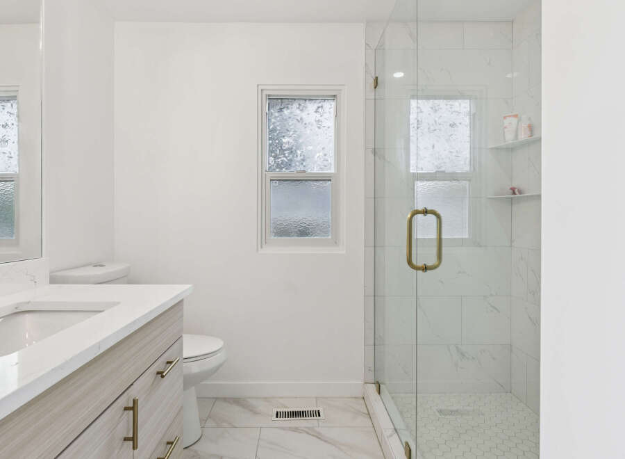 Experience modern luxury in this stunning bathroom featuring a sleek vanity with a quartz countertop and elegant brass hardware.