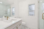 This modern bathroom features a sleek vanity with a quartz countertop and gold fixtures, complemented by a large mirror and a spacious glass-enclosed shower with marble tile.