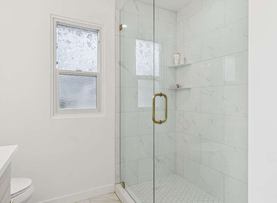 Experience modern elegance in this bathroom featuring a sleek glass-enclosed shower with marble-look tiles and a chic hexagonal floor.