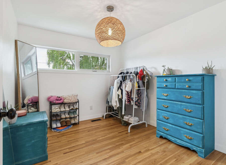 Bright and airy bedroom featuring a large window with natural light, a stylish woven pendant light, and a vibrant teal dresser.
