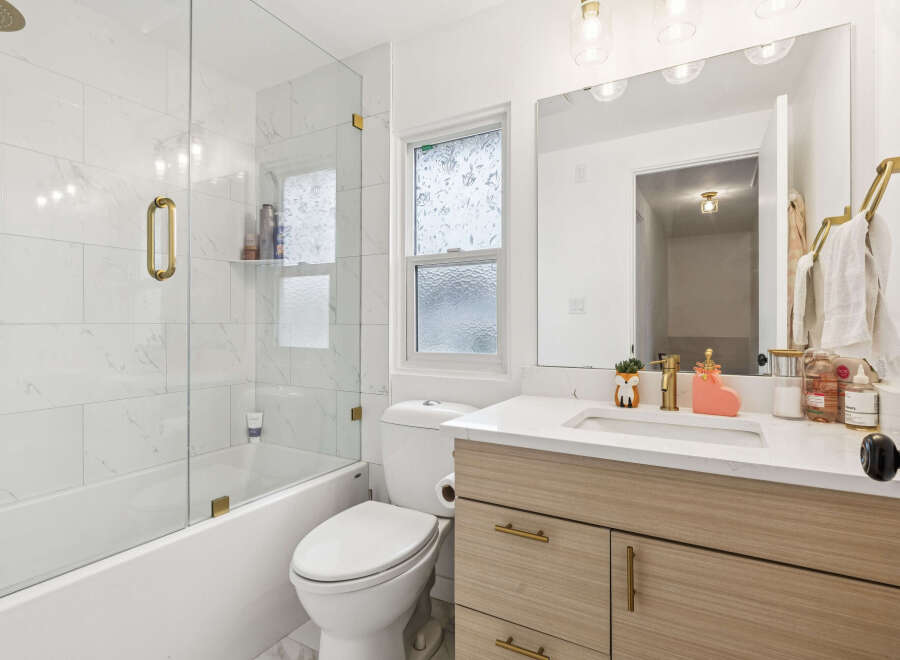 This modern bathroom features a sleek design with marble-look tile walls and a glass shower enclosure.
