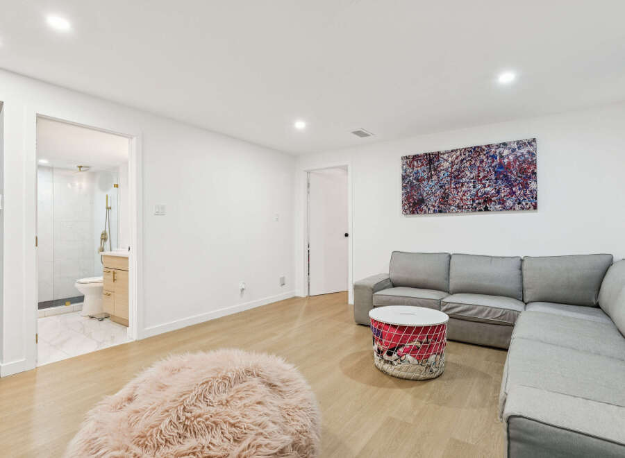This modern living space features a comfortable grey sectional sofa complemented by a unique wire basket coffee table and a plush pink accent pouf.
