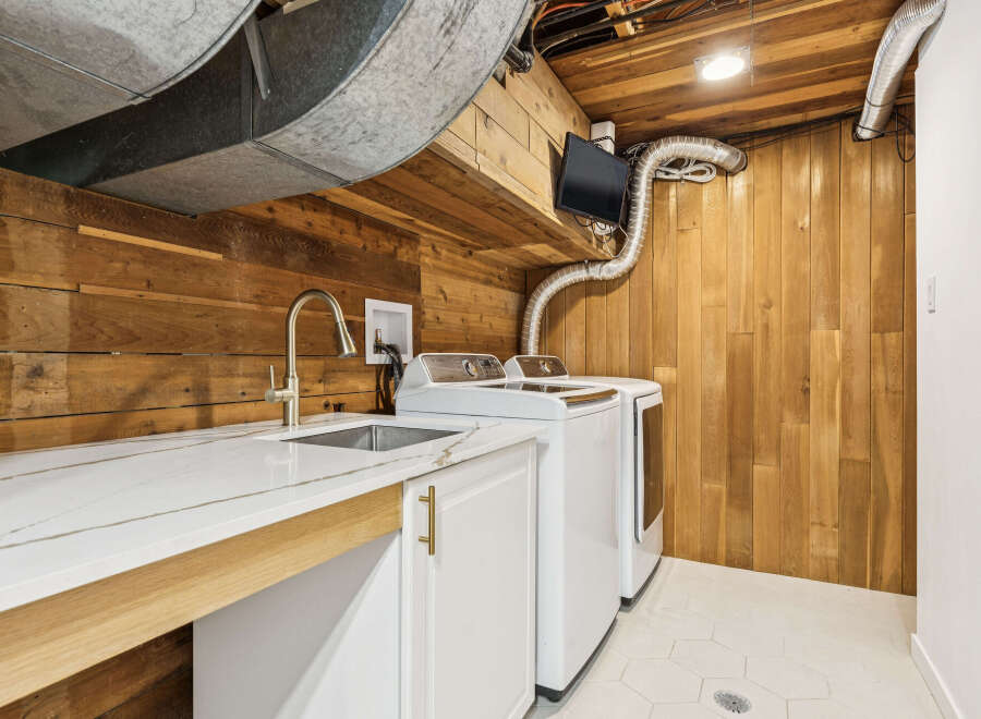 This laundry room features a modern white quartz countertop with a sleek stainless steel sink and faucet, complemented by white cabinetry with gold hardware.