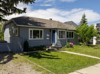 Charming grey bungalow with a welcoming blue front door and pristine white trim.
