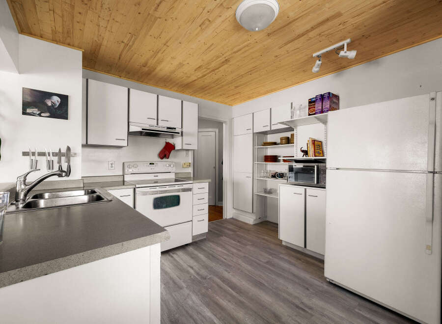 Discover this charming kitchen featuring a spacious double sink, a white electric stove, and ample cabinet space for all your culinary needs.