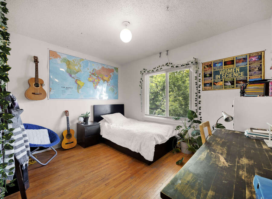 Discover a vibrant and inspiring bedroom featuring a world map, two acoustic guitars, and a cozy reading nook with a blue chair.