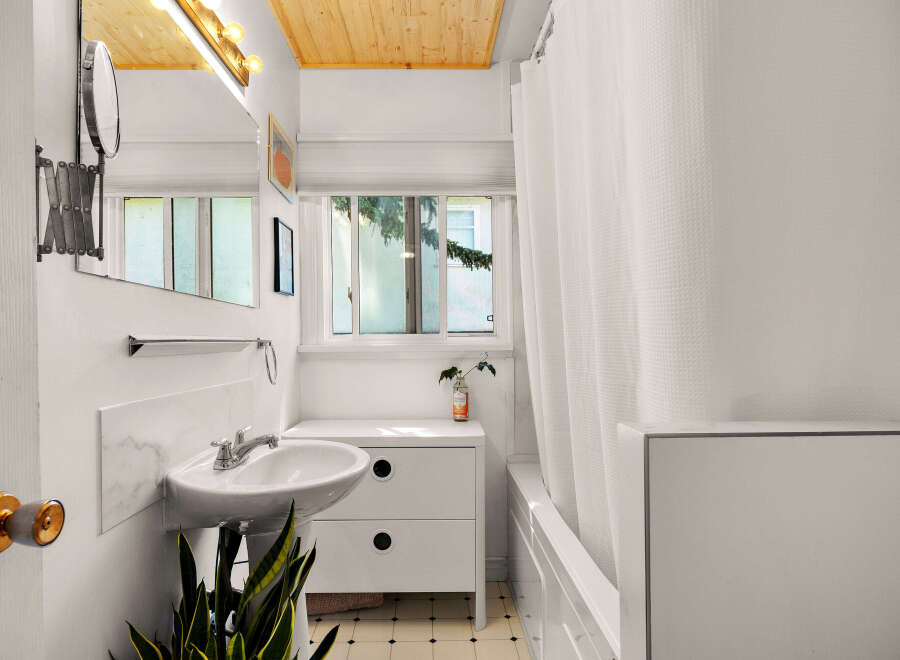 This charming bathroom features a pedestal sink with a marble backsplash and a magnifying mirror, perfect for your morning routine.