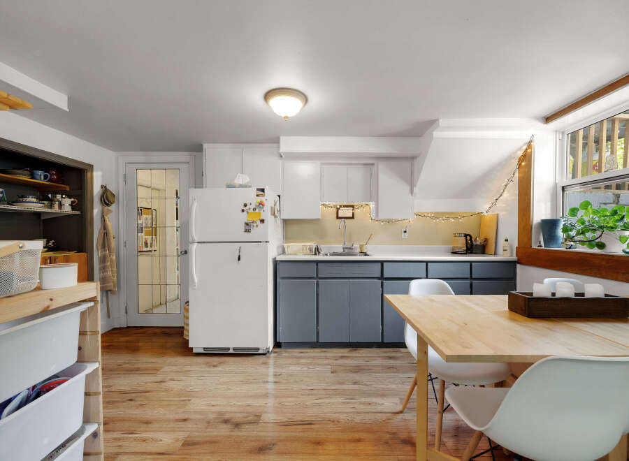 Discover this charming kitchen featuring a bright white refrigerator, sleek gray cabinetry, and a cozy dining area with a light wood table and white chairs.