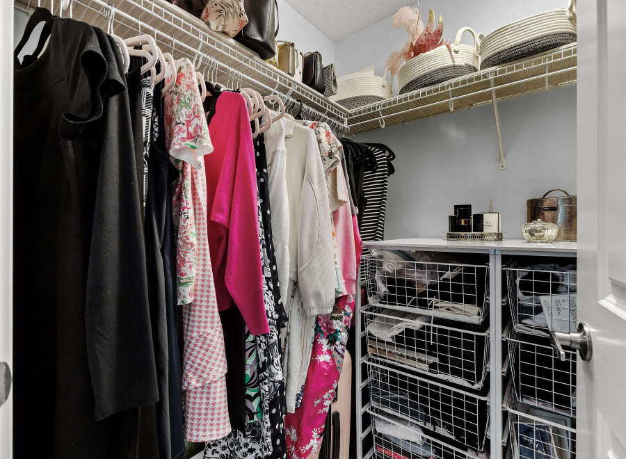 Discover organized living in this spacious walk-in closet, featuring ample hanging space for your wardrobe and convenient wire basket storage for accessories.