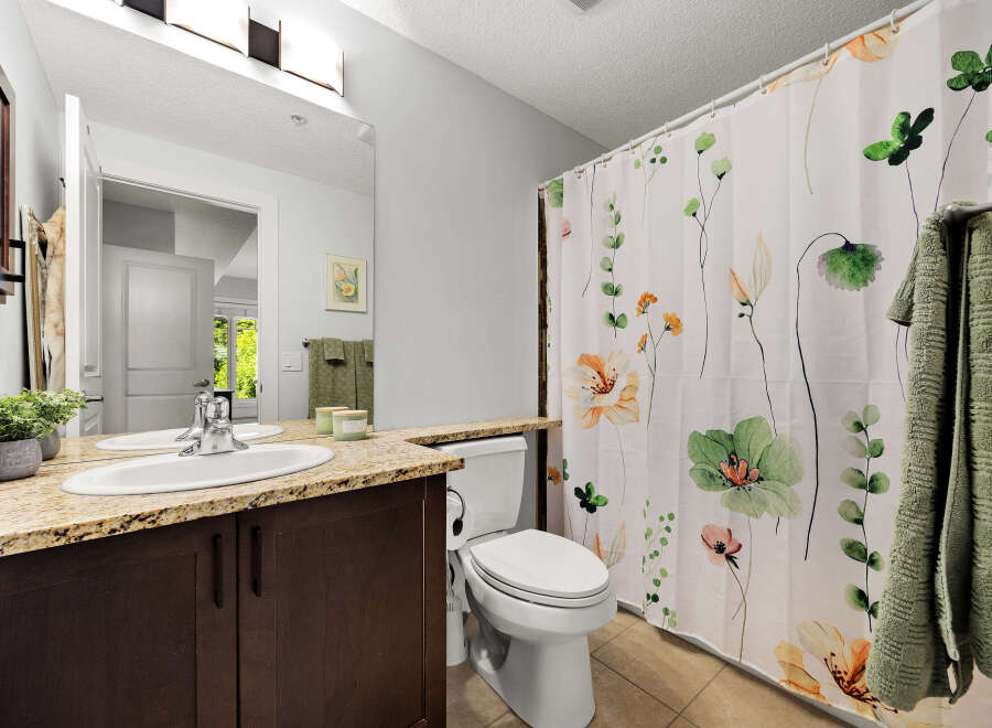 This bathroom features a modern vanity with a granite countertop and a double sink, complemented by a floral shower curtain.