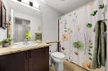 This bathroom features a modern vanity with a granite countertop and a double sink, complemented by a floral shower curtain.