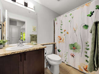 This bathroom features a modern vanity with a granite countertop and a double sink, complemented by a floral shower curtain.
