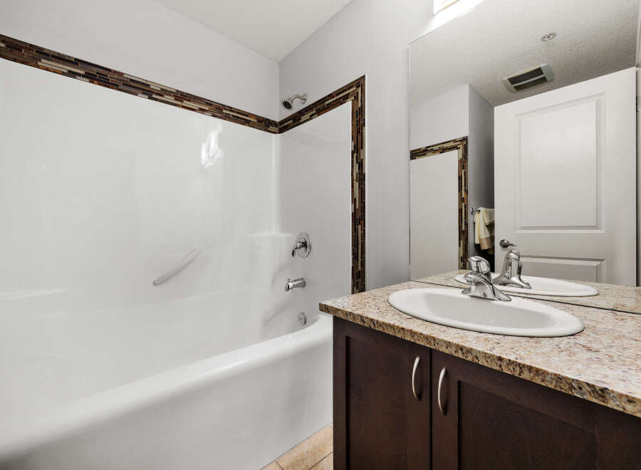 This bathroom features a pristine white bathtub with a decorative mosaic tile accent along the top edge, complemented by a sleek chrome showerhead and faucet.