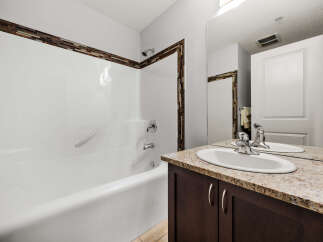 This bathroom features a pristine white bathtub with a decorative mosaic tile accent along the top edge, complemented by a sleek chrome showerhead and faucet.