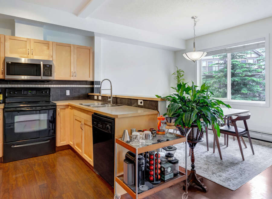 This modern kitchen features light wood cabinetry, a sleek black appliance suite including a microwave and dishwasher, and a double sink with a gooseneck faucet.