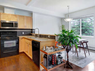 This modern kitchen features light wood cabinetry, a sleek black appliance suite including a microwave and dishwasher, and a double sink with a gooseneck faucet.