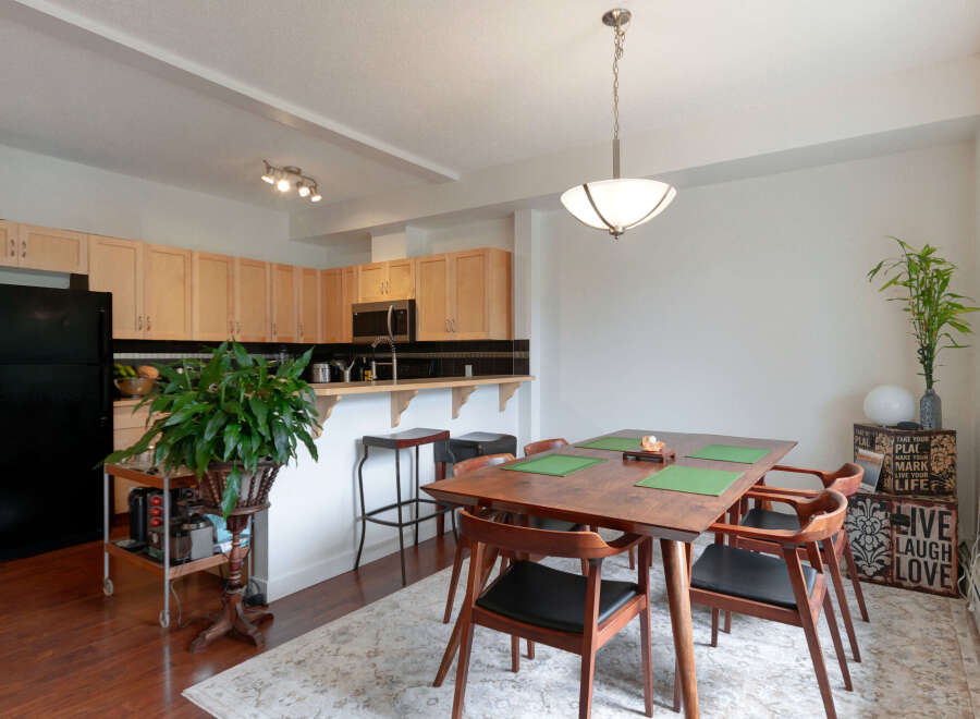 This open-concept living space features a modern kitchen with light wood cabinetry and a sleek black backsplash, seamlessly flowing into a dining area.