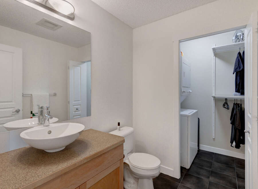 This modern bathroom features a sleek vanity with an undermount sink and a chrome faucet, complemented by a large mirror reflecting a clean white door.