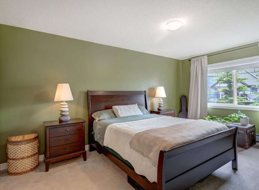 This inviting bedroom features a dark wood sleigh bed with crisp white and green bedding, complemented by matching dark wood nightstands with unique stacked stone lamps.