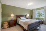 This inviting bedroom features a dark wood sleigh bed with crisp white and green bedding, complemented by matching dark wood nightstands with unique stacked stone lamps.