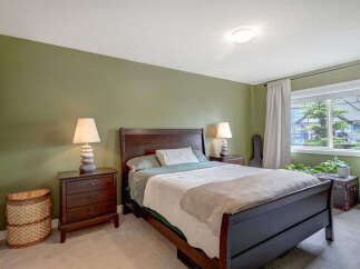 This inviting bedroom features a dark wood sleigh bed with crisp white and green bedding, complemented by matching dark wood nightstands with unique stacked stone lamps.