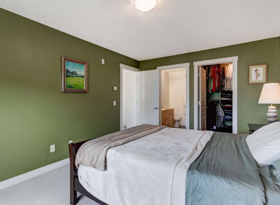This inviting bedroom features a spacious bed with comfortable bedding, complemented by a serene green accent wall.