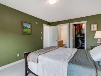 This inviting bedroom features a spacious bed with comfortable bedding, complemented by a serene green accent wall.