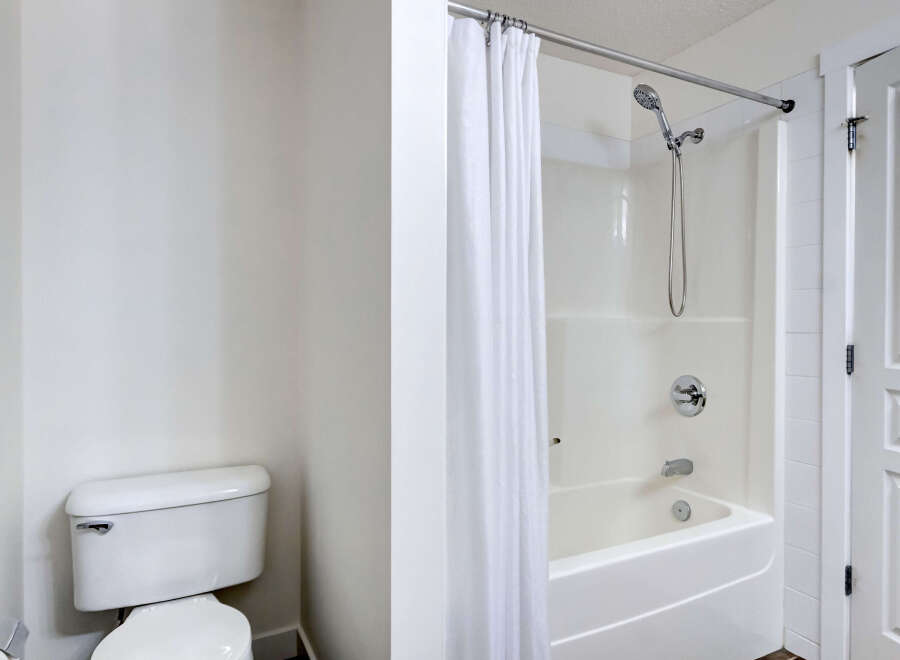 This bathroom features a pristine white toilet and a modern shower/tub combination with a sleek chrome showerhead and faucet.